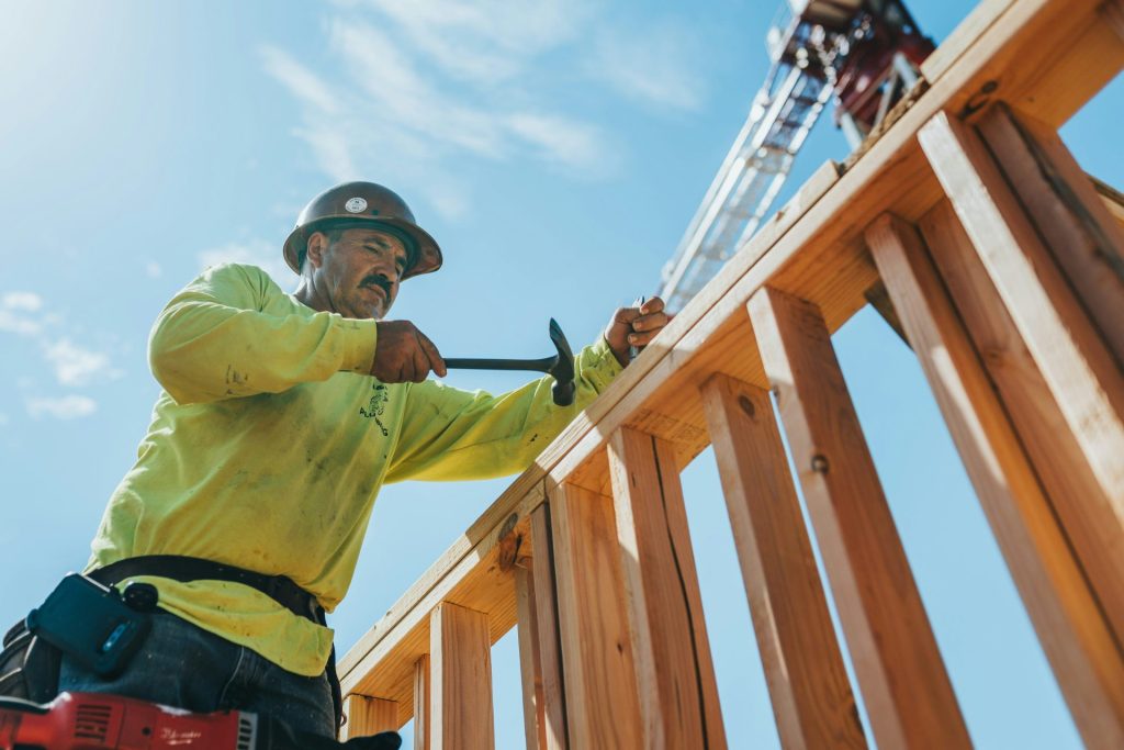 Ein Mann mit Schutzhelm und Sicherheitsausrüstung, der an einer Holzkonstruktion arbeitet.